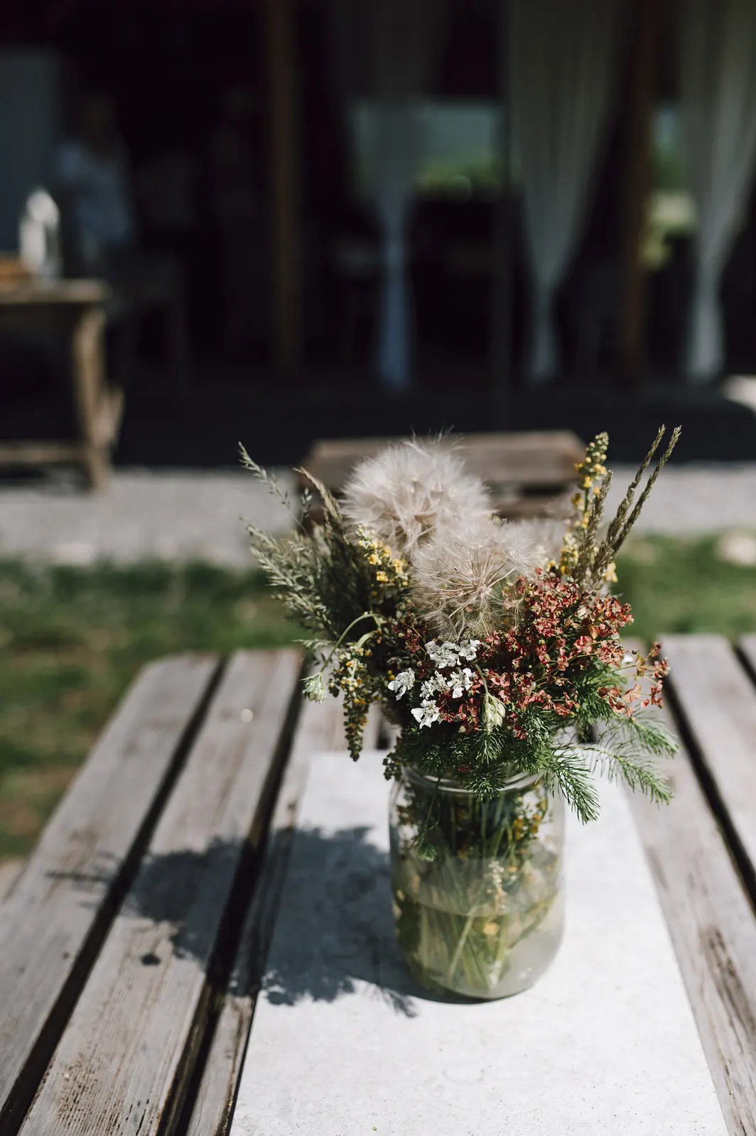 Wildflowers in a glass jar on a wooden table outdoors