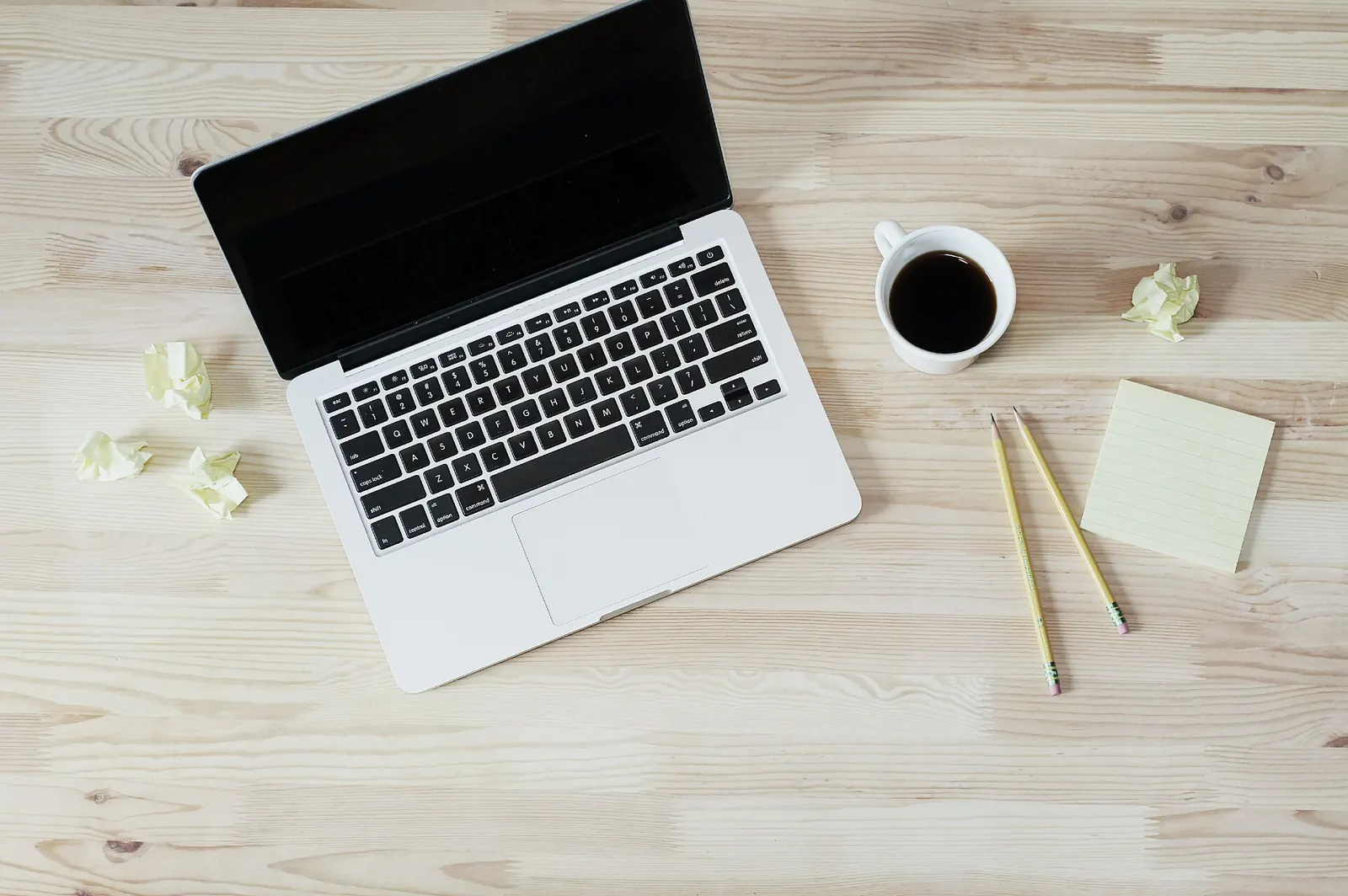 A laptop, a cup of coffee and notes on a wooden table